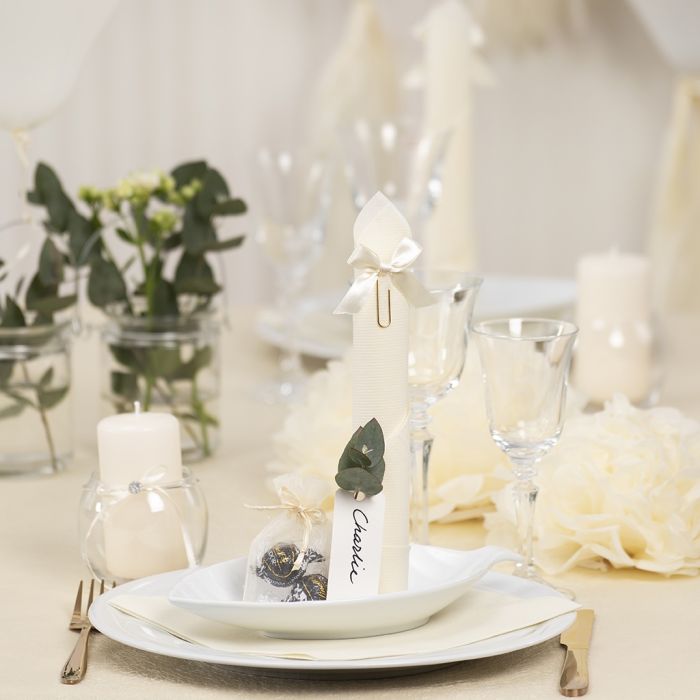 Décorations de table blanc cassé avec des fleurs en papier, des ballons, une serviette pliée en forme de tour et des marque-places.