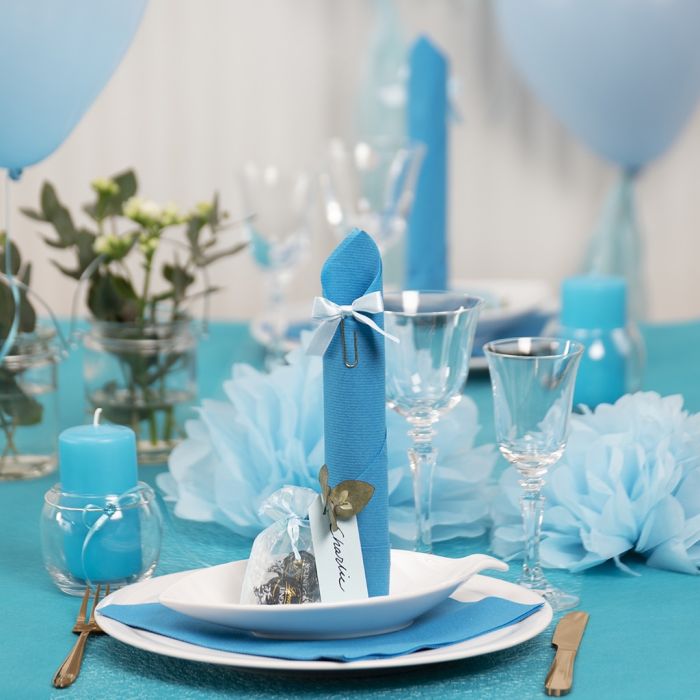 Décorations de table bleu clair avec des fleurs en papier, des ballons, une serviette pliée en forme de tour et des marque-places.