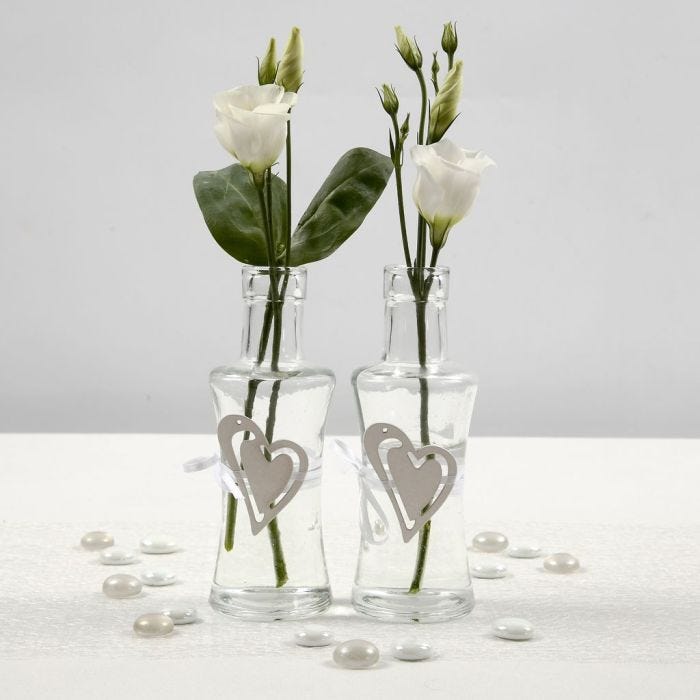 Un vase en verre décoré d'un coeur en bois fixé avec une ceinture en ruban de satin blanc